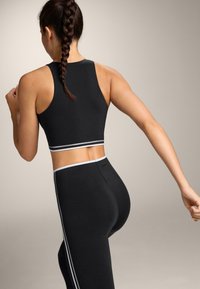 Black sports crop top and leggings with white side stripes. Tight-fitting, smooth material; racerback design highlights shoulder and back.