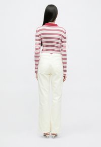 Langærmet top med røde og hvide striber, kombineret med hvide, vidde bukser med høj talje. Toppen har en glat tekstur og ribstrikkede detaljer.