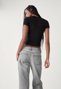 Un haut noir à manches courtes ajusté associé à un jean gris clair taille moyenne avec une coupe décontractée et de discrets détails de coutures sur les poches arrière.