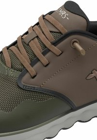 Ingrandimento di una sneaker marrone e verde con tessuto testurizzato, lacci marroni, collare imbottito nero e suola bianca ondulata.