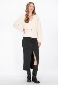 Light cream cardigan with a soft texture, belted in white, paired with a black denim skirt featuring a front slit, and knee-high black boots.