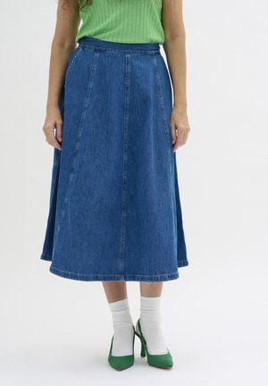 Jeansrock in A-Linie mit hoher Taille, blauer Farbe, gepflücktem Design und gesäumten Kanten; kombiniert mit grünen Absätzen und weißen Socken.