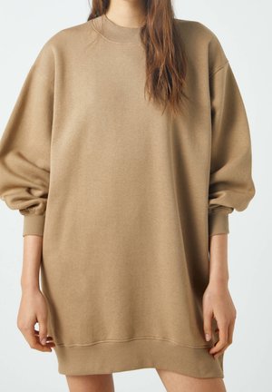 Robe sweat-shirt beige surdimensionnée en tissu doux, dotée d'un col rond, de manches longues bouffantes et de poignets côtelés. Design minimaliste sans motifs.