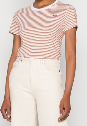 Osoba nosząca biało-pomarańczowy, krótki rękaw t-shirt marki Levi's, zestawiony z jasnobeżowymi spodniami z wysokim stanem.