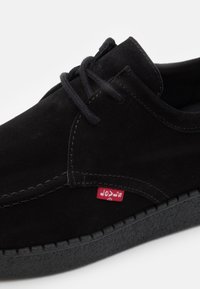 Černé z semišové kůže se šněrováním, s texturovanou podrážkou a malou červenou látkovou štítkem našitým na boku.