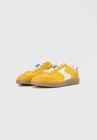 Para żółto-białych niskoprofilowych sneakersów z niebieskimi akcentami, białymi sznurowadłami, bocznym zamkiem błyskawicznym i gumowymi podeszwami na białym tle.