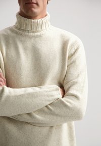 Cremfarbener Strickpullover mit hohem Rippkragen, strukturiertem Stoff und gerippten Bündchen; lockere Passform und dezentes meliertes Muster.