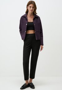 Paarse cropped jack met borstzakken, zwart cropped top, op maat gemaakte zwarte broek en zwarte loafers met kwastaccenten. Strakke lijnen, moderne pasvorm.