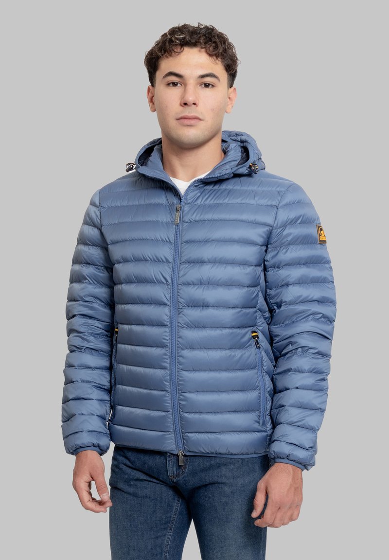 Giacca a vento imbottita azzurro chiaro con cappuccio con cerniera, trapuntatura orizzontale e tasche laterali con zip. Presenta una toppa con logo sulla manica. Texture liscia.