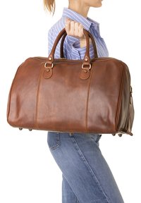 Borsa da viaggio in pelle marrone con doppie maniglie, cuciture dettagliate e hardware in ottone. Forma strutturata con estremità arrotondate e piedini per stabilità.