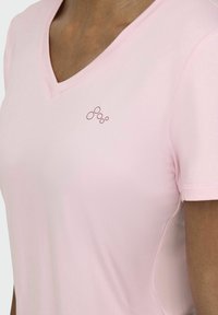 Camiseta de cuello en V en color rosa claro, hecha de una tela suave, con mangas cortas y un sutil logo de tres círculos en un rosa más oscuro en el pecho.