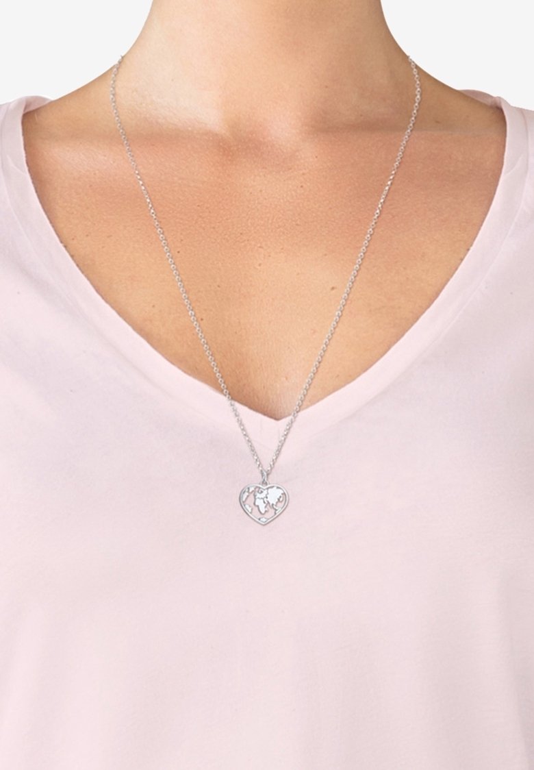 Collier chaîne argent avec pendentif en forme de cœur présentant une carte du monde, porté avec un t-shirt à col en V rose clair.