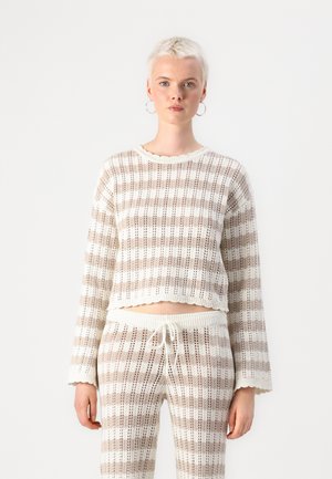 Cream and light brown striped cropped sweater with a textured knit design, featuring long sleeves and a scalloped hem. Paired with matching pants.