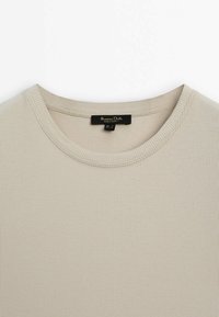 T-shirt beige côtelé à col rond avec une étiquette noire Massimo Dutti cousue à l'intérieur de l'encolure.