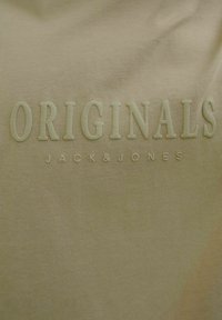Olivinės spalvos medvilninis marškinėliai su tekstūruotu audiniu; su reljefiniais "ORIGINALS" ir "JACK & JONES" logotipais tos pačios spalvos.
