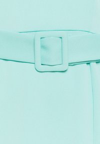 Ljusblått tyg med en slät textur. Ett bälte med en fyrkantig spänne drar åt midjan, vilket framhäver plaggets form och struktur.