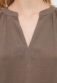 Καφέ μπλούζα με V-λαιμόκοψη, απαλής υφής και διακριτικές ραφές. Διαθέτει στρογγυλεμένους ώμους για επιπλέον στυλ.