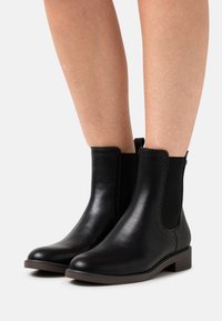 Botines de cuero negro con paneles elásticos en los costados, puntera redondeada y un tacón bajo. Presentan costuras decorativas a lo largo de los bordes.
