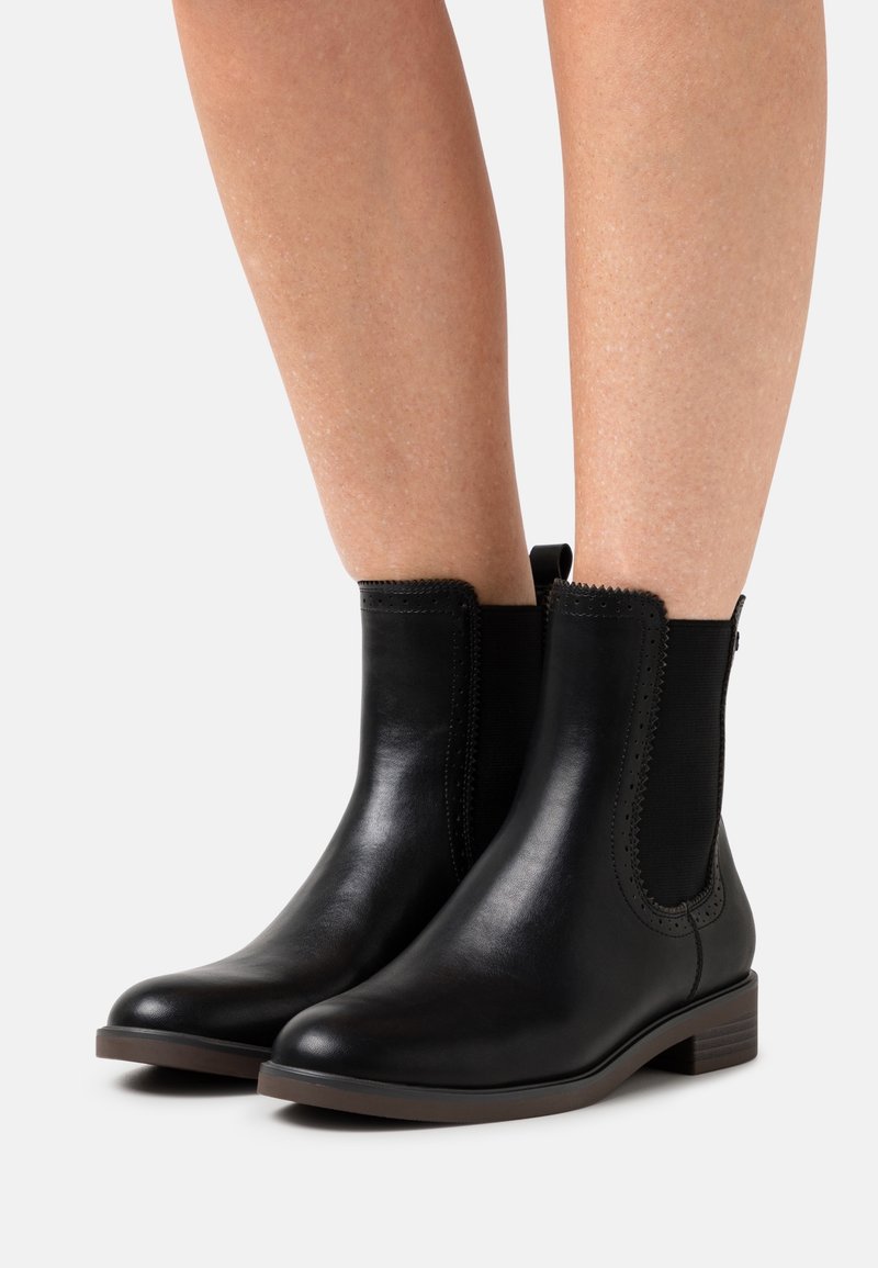 Botines de cuero negro con paneles elásticos en los costados, puntera redondeada y un tacón bajo. Presentan costuras decorativas a lo largo de los bordes.