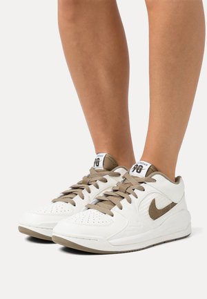 Baskets Nike Air Jordan blanches et beiges portées pieds nus, montrant les vues latérale et avant avec les lacets noués.