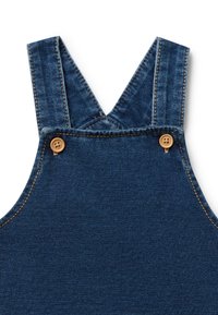 Salopette in denim con bretelle regolabili, chiusura in legno, tessuto blu scuro con texture sottili e dettagli di cucitura a contrasto.
