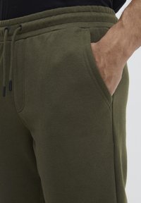 Olivgrüne Jogginghose mit elastischem Bund und Kordelzug, ausgestattet mit Seitentaschen und einem weichen, strukturierten Stoff.