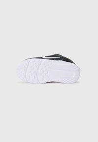 Schwarzer Sportschuh mit einer strukturierten Oberseite, ausgestattet mit einem weißen Swoosh-Logo und einer weißen Gummisohle mit Profilmuster.