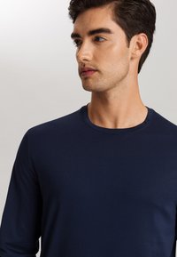 Camisa de manga larga azul marino con escote redondo, fabricada en tejido suave; presenta una silueta ajustada con un mínimo detalle de costura.