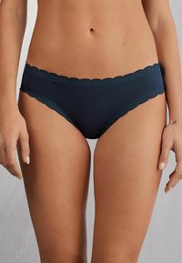 Navyblauwe onderbroek met een gekartelde kantafwerking aan de taille. Zacht materiaal met een gladde textuur, in een klassieke slipstijl.