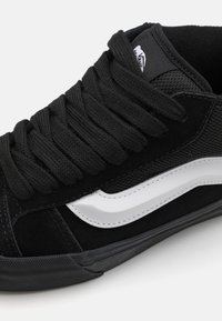 Sneaker in suede nero con lacci spessi neri, motivo a striscia a onda bianca e dettagli in mesh testurizzato sulla parte superiore. Suola in gomma.