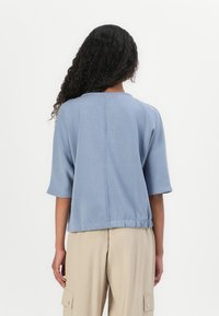 Top azul de mangas curtas com decote redondo e bainha ajustada. Feito de um tecido macio com uma textura leve e acabamento suave.
