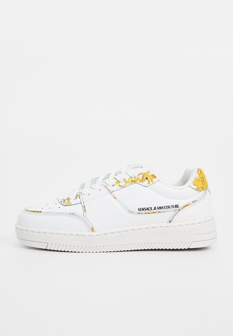Zapatillas de cuero blancas con acentos florales dorados, con una suela texturizada y diseño de cordones. Logo de la marca visible en el lateral.