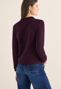 Paarse geribbelde top met lange mouwen en een ronde hals, gecombineerd met blauwe spijkerbroek met achterzakken en een rechte pasvorm.