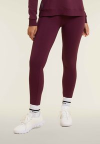 Leggings bordeaux realizzati in tessuto elasticizzato, con un design affusolato. Abbinati a scarpe da ginnastica bianche e calzini a righe bianche e nere.