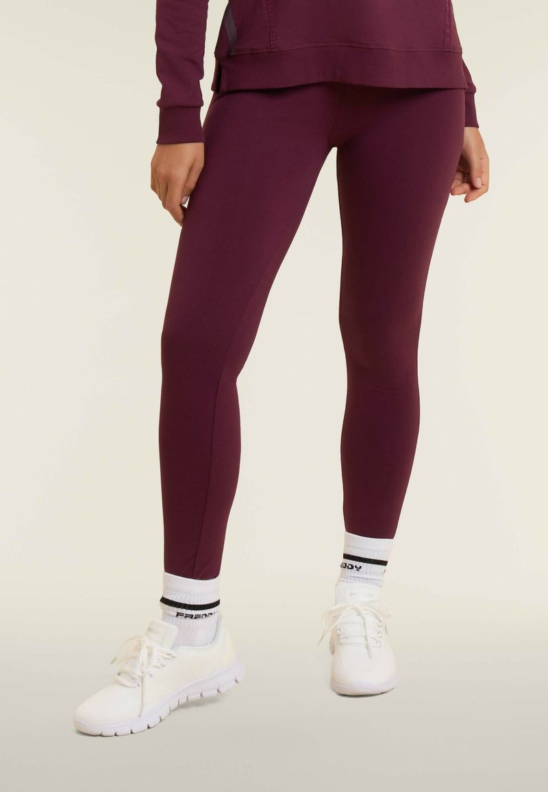 Leggings bordeaux realizzati in tessuto elasticizzato, con un design affusolato. Abbinati a scarpe da ginnastica bianche e calzini a righe bianche e nere.