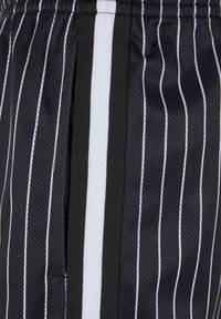 Shorts de sport noirs à fines rayures blanches, présentant une texture en maille respirante et des accents verticaux le long des poches latérales.