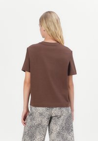 Brun bomulls t-skjorte med rund hals, korte ermer og løs passform, kombinert med beige leopardmønstrede bukser.