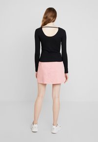 Musta ribbimallin pitkähihaista toppia, jossa on leveä selkäaukko, yhdistettynä vaaleanpunaiseen farkku-mekkoon. Mallilla on valkoiset tennarit.