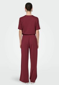 Bordeaux jumpsuit med en afslappet pasform, korte ærmer, elastisk talje, brede ben og subtile sidelister. Glat stof med en let glans.