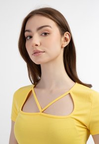 Top ribbed galben cu decolteu pătrat, design crisscross, mâneci scurte și o siluetă ajustată. Textură netedă.