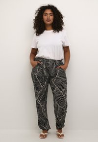 Schwarz-weiße gemusterte Hose mit lockerer Passform, elastischem Bund und seitlichen Taschen. Kombiniert mit einem schlichten weißen T-Shirt und Sandalen.