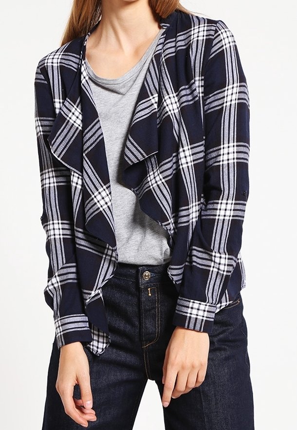 Navyblårandig kavaj med draperad front, långa ärmar och mjukt tyg, lager på lager över en grå skjorta och mörka jeans.