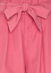 Pantalons en tissu rose avec une ceinture nouée à la taille, au texture lisse, avec des poches latérales et des coutures contrastantes.