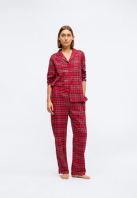 Rødternet pyjamassæt bestående af en skjorte med knapper, krave og lange ærmer, parret med løstsiddende bukser og en bundet talje.