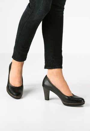 Escarpin en cuir noir avec un bout arrondi, un design à décolleté bas et un talon modéré. Texture lisse avec des détails de couture discrets au niveau de la semelle.