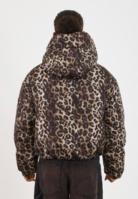 Polstret leopardmønstret jakke med hætte og blank finish. Har et mønster af mørkebrun og lys brun pletter på en beige baggrund.