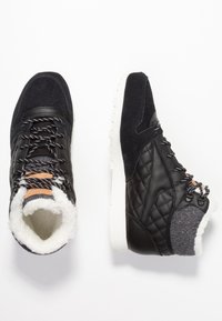 Svart quiltade vinterstövlar med vit pälsinredning, snörning fram, mockatå och grå knittrad ankelflik som visas från ovan- och sidovy.