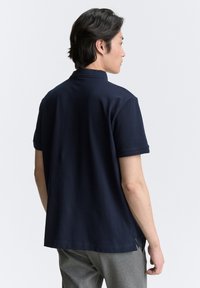 Navyblauw polo shirt met korte mouwen, een klassieke kraag, zijsplitten en een gladde, zachte textuur. Draagt bij grijze broeken.