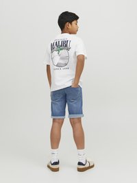Vit t-shirt med grafiken "Malibu California", kombinerad med upprullade denimshorts. Vita strumpor och skor med mörka accenter fulländar looken.