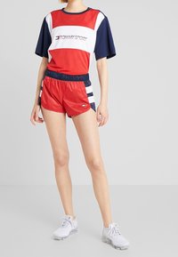 Czerwono-niebiesko-biała sportowa stylizacja składająca się z krótkiego rękawa koszulki z siateczki z logo oraz czerwonych szortów z granatowymi paskami. Uzupełniona białymi trampkami.